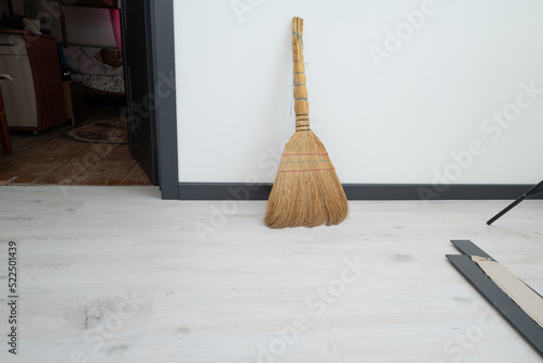 A straw broom on a white wall background.