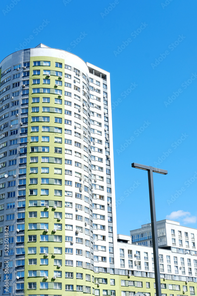 Fototapeta premium Multi-storey building in the form of a cylinder and painted in white and green colors against a blue sky.