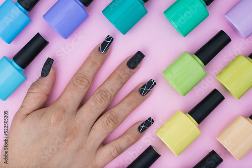 top view of a girl's hand with nails painted black with white. pattern of enamels of different colors placed on a pink, purple, blue, green and yellow background. elements to make a nail painting