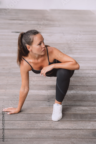 A sporty woman in sportswear is doing fitness on wooden floor.
