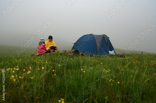 Mother and daughter sit near the tent after the rain  family vacation in the mountains.