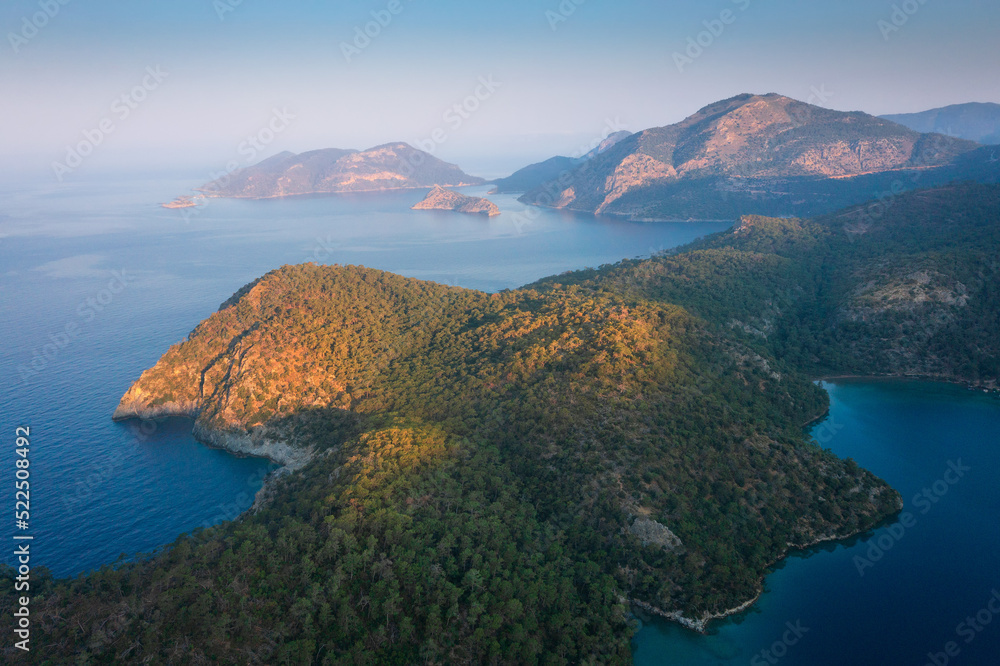 Aerial view of morning seascape and moutain islands. The sun rises gradually over islands. Sun rays illuminate blue lagoon in Mediterranean, Turkey.