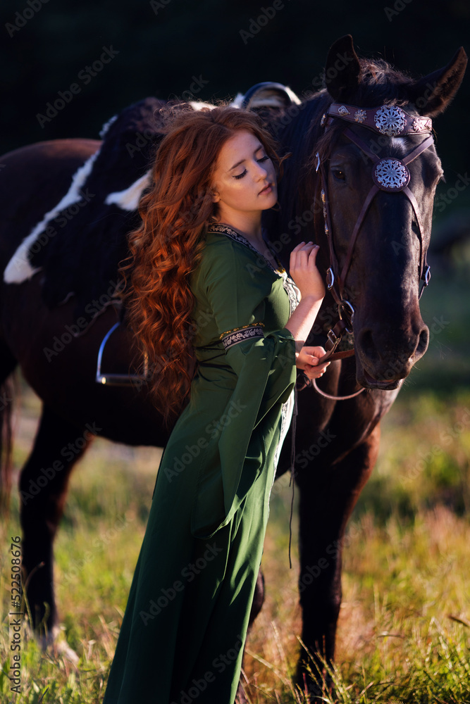 Naklejka premium Medieval woman princess in green dress sits astride black steed horse.