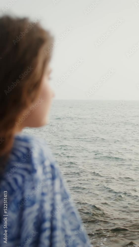 A woman smiles looking into the distance, sitting on boulders on the seashore A woman smiles looking into the distance, sitting on boulders on the seashore
