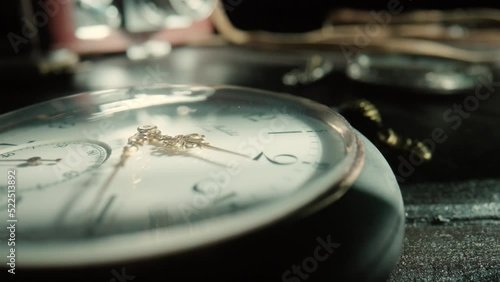 Silver antique pocket watch with ticking gold hands and vintage camera in background. An old round dial of a pocket watch lying on a dark wooden table. Running clock hands in circle. Close up.