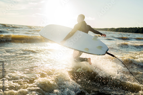 A male surfer goes in for sports at sea uses a surfboard in a wetsuit