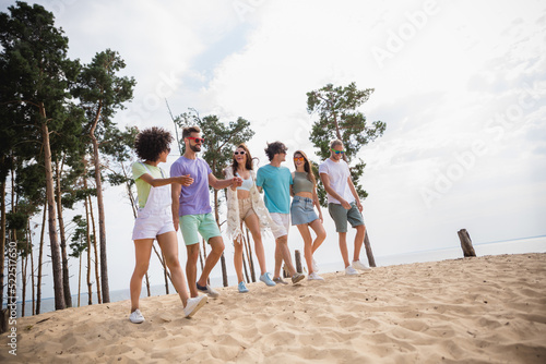 Photo of charming funky buddies company smiling walking holding arms outdoors countryside sea forest