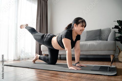 Asian chubby woman sitting on the floor in living room practice online yoga lesson with the computer. female having meditate training class on the laptop..