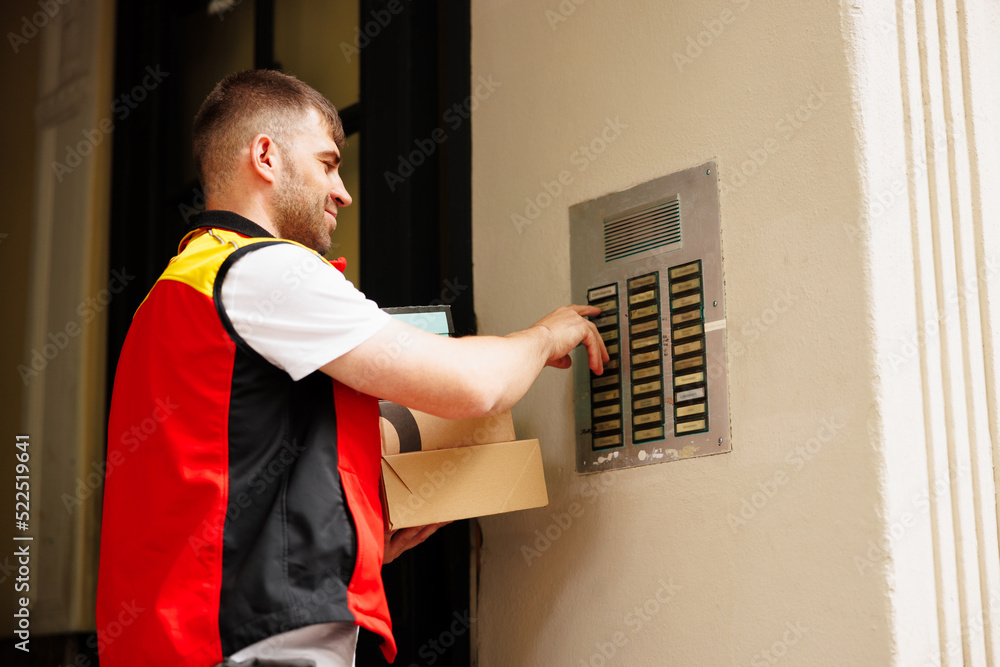 Delivery man pressing button of intercom to enter building