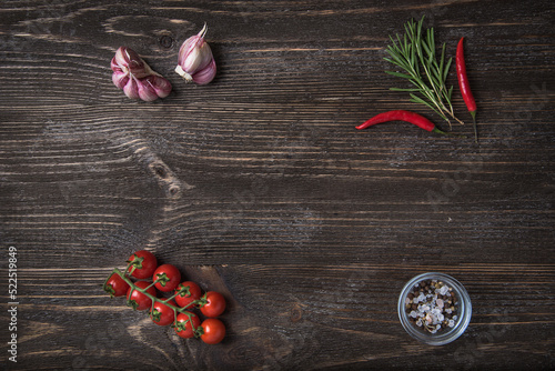 Wooden background with vegetable decor: cherry tomatoes, garlic, rosemary and chilli peppers