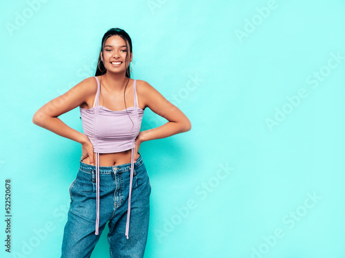 Young beautiful smiling female in trendy summer jeans and top clothes. Carefree woman posing near blue wall in studio. Sexy positive model having fun indoors. Cheerful and happy