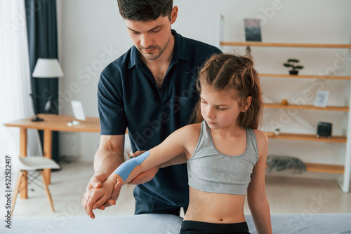 Professional physiotherapist putting kinesio tape on kid arms in clinic
