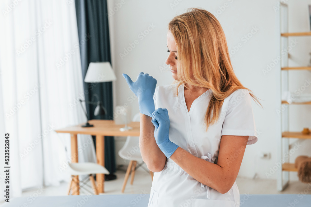 Wearing gloves. Female doctor in white coat is standing in the clinic Wearing gloves. Female doctor in white coat is standing in the clinic