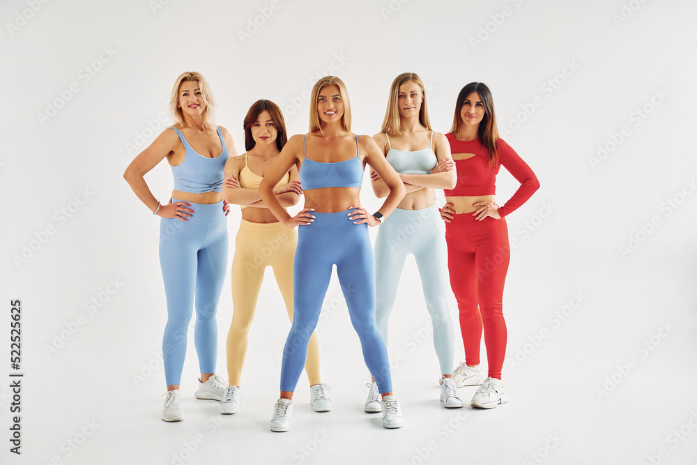 Naklejka premium Standing against white background with arms on waist. Beautiful women in sportive clothes is indoors in the studio