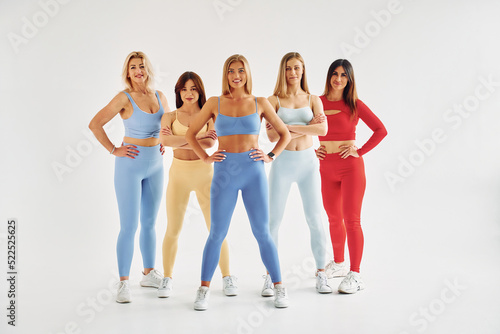 Standing against white background with arms on waist. Beautiful women in sportive clothes is indoors in the studio
