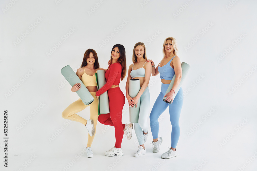 Obraz premium Standing with yoga mats in hands. Beautiful women in sportive clothes is indoors in the studio