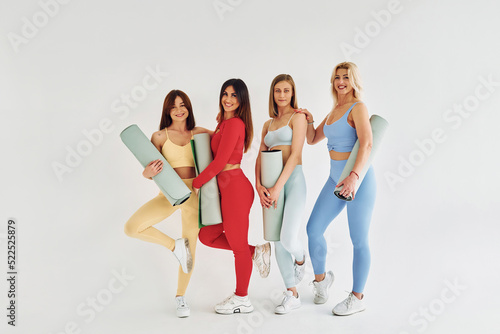 Standing with yoga mats in hands. Beautiful women in sportive clothes is indoors in the studio