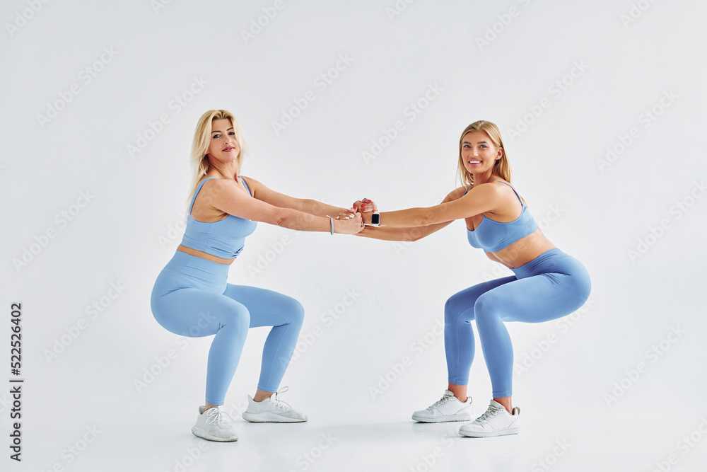 Fototapeta premium Doing squats. Beautiful women in sports clothes is indoors in the studio