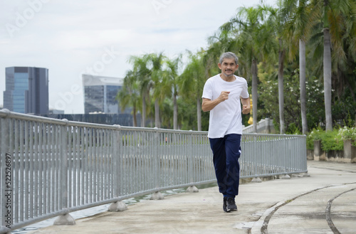 asian senior man running along walkway in the city park