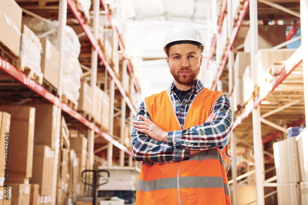 Standing with arms crossed. Employee in uniform is working in the storage at daytime Standing with arms crossed. Employee in uniform is working in the storage at daytime