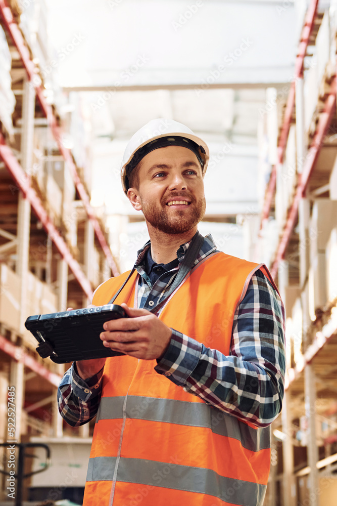Obraz premium With tablet. Employee in uniform is working in the storage at daytime