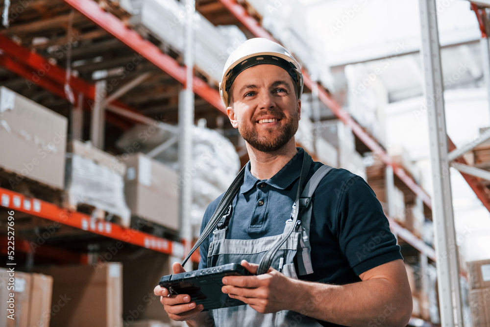 Obraz premium With digital tablet in hands. Employee in uniform is working in the storage at daytime