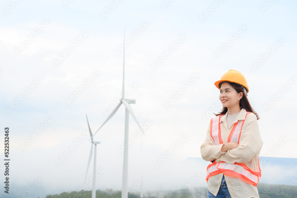 Young woman engineer with windmill at a renewable energy generating station in a windmill field. Young woman engineer with windmill at a renewable energy generating station in a windmill field.