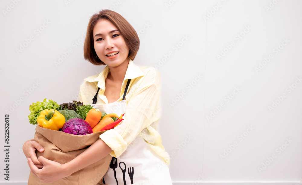 Young smiling Asian cheerful happy fun vegetarian woman 20s in casual clothes hold paper bag with vegetables after shopping look camera isolated on plain yellow background studio portrait. Young smiling Asian cheerful happy fun vegetarian woman 20s in casual clothes hold paper bag with vegetables after shopping look camera isolated on plain yellow background studio portrait.