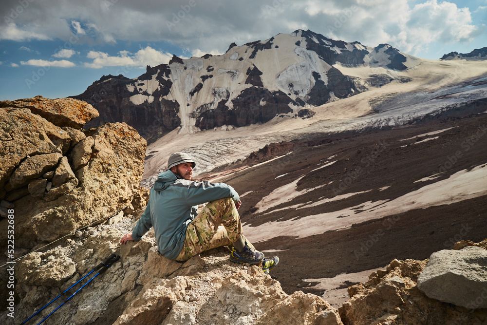 Man sitting over Mt Kazbeg base camp and enjoying view of Gergeti glacier. Meteostation in Kazbek, Georgia. Mount kazbek alpinist expedition Man sitting over Mt Kazbeg base camp and enjoying view of Gergeti glacier. Meteostation in Kazbek, Georgia. Mount kazbek alpinist expedition