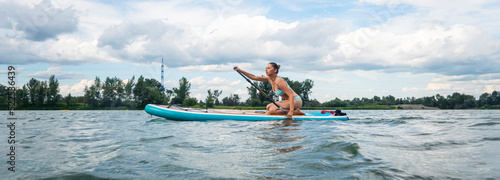 Caucasian woman is riding a SUP board on the river in city. Summer sport. panorama photo