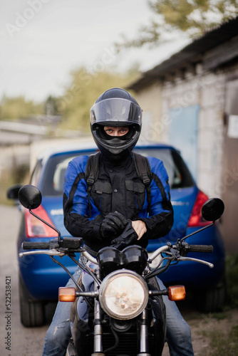 male motorcyclist in a helmet and gear puts on leather gloves.