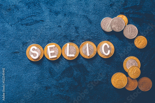 Selic. A palavra Selic escrita com letras brancas sobre moedas do Real Brasileiro - BRL, dinheiro do Brasil. Moedas de 1 Real em fundo azul. photo