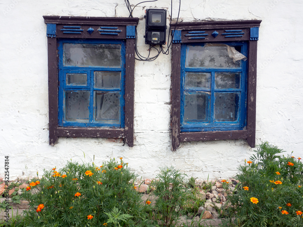 Old rural Ukrainian house. White Wall with blue windows.