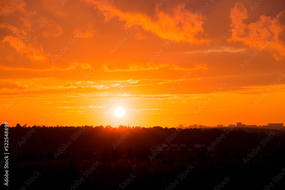 Obraz premium Banner. Beautiful red-orange fiery sunset over the city. Dark clouds in the sky. The outlines of skyscrapers on the horizon.