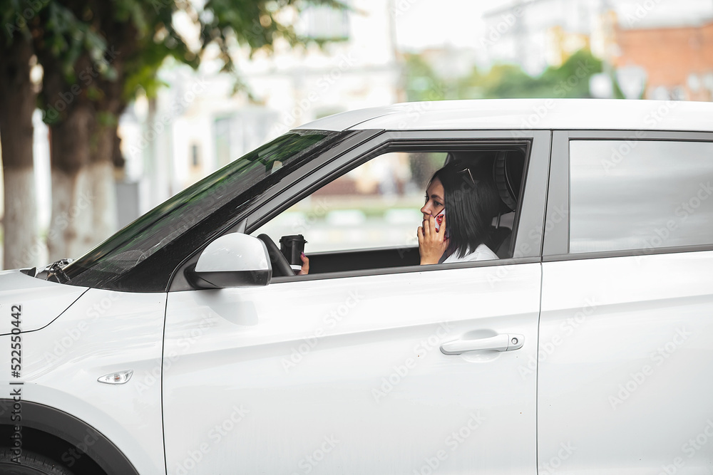 young beautiful brunette woman driver sitting in her car with a glass of coffee and talking on the phone