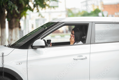 young beautiful brunette woman driver sitting in her car with a glass of coffee and talking on the phone © Ольга Рязанцева