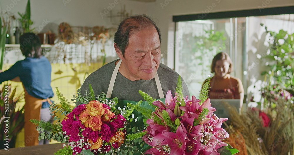 Asian American business entrepreneur owner of flower shop standing holding two bouquet of flower arrangements smiling at camera. Small business concept
