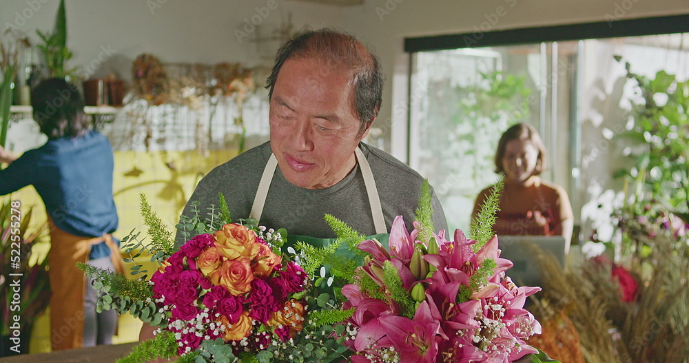Asian American business entrepreneur owner of flower shop standing holding two bouquet of flower arrangements smiling at camera. Small business concept
