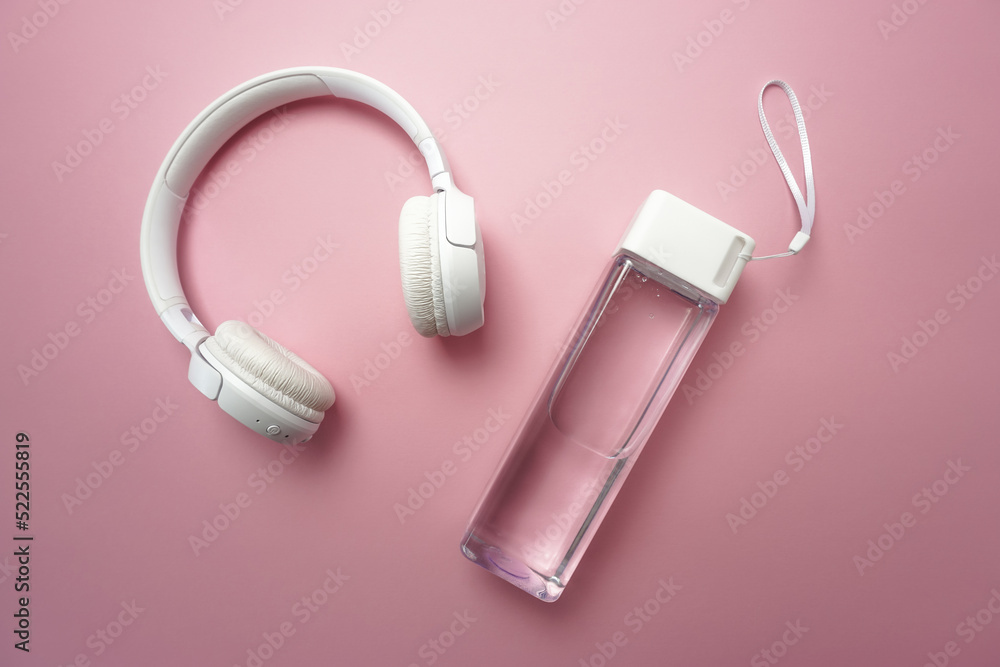 On a pink background there is a bottle of clean water and white headphones On a pink background there is a bottle of clean water and white headphones