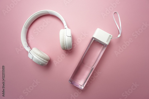 On a pink background there is a bottle of clean water and white headphones 