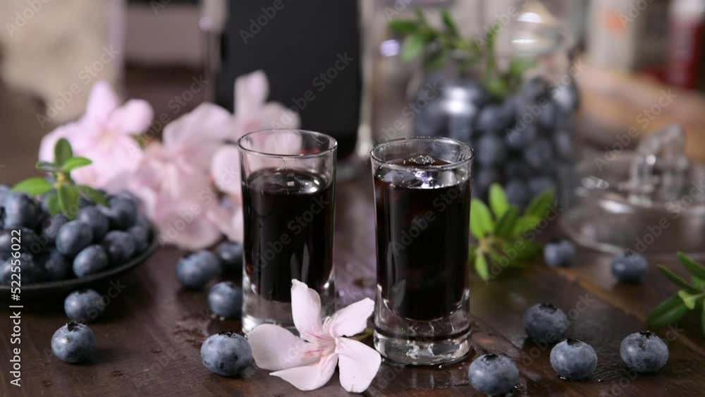 Mirto liqueur. A traditional blueberry liqueur from Sardinia, Italy. Sweet and aromatic drink at the end of the meal. Two small glasses with an alcoholic drink on the table and blueberries. slowmotion Mirto liqueur. A traditional blueberry liqueur from Sardinia, Italy. Sweet and aromatic drink at the end of the meal. Two small glasses with an alcoholic drink on the table and blueberries. slowmotion