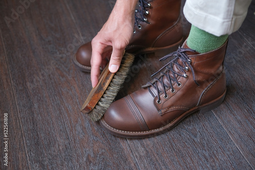close up of hand of person with shoe brush that cleans casual leather brown boot