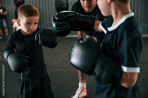 Having fun by practicing. Young tattooed coach teaching the kids boxing techniques © standret