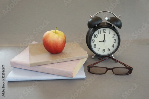 Stack of Three Books, Red & Yellow Apple, Black Alarm Clock and Glasses