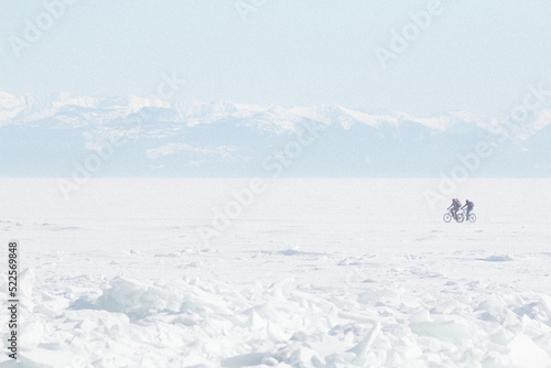  two cyclists ride on the frozen lake Baikal. Early spring in Siberia © Sergey