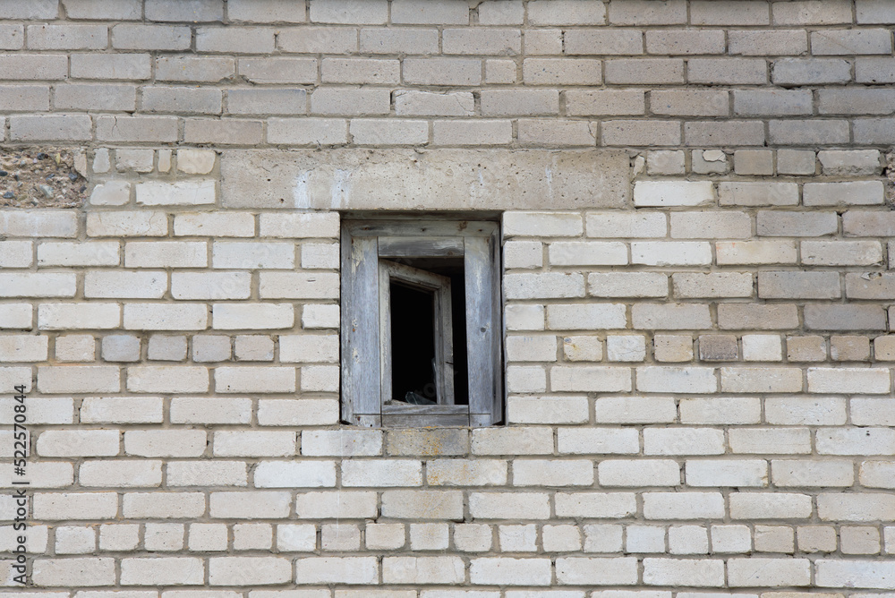 wall of a white brick building with a broken open small window on a cloudy day