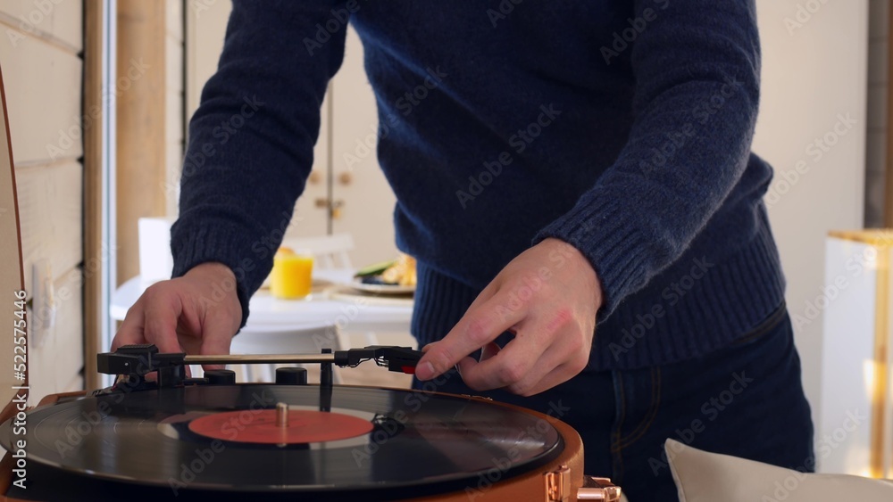 A man puts a vinyl record into a player and turns it on. The record spins and the man lowers the needle to read the music. Listening to music at home alone, classical music from the gramophone. A man puts a vinyl record into a player and turns it on. The record spins and the man lowers the needle to read the music. Listening to music at home alone, classical music from the gramophone.