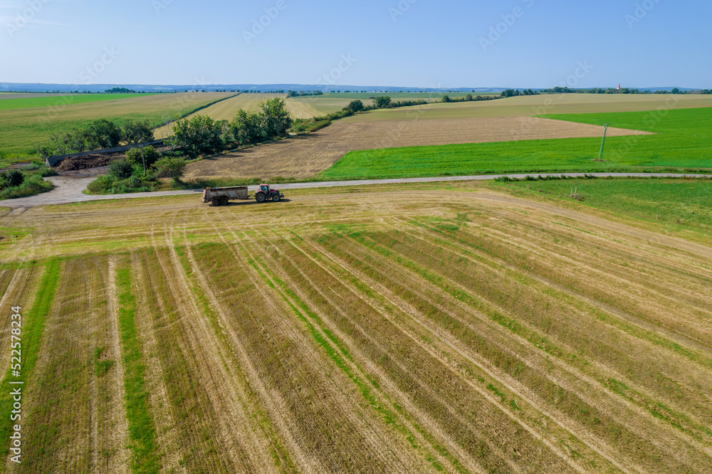 Top view of a tractor moving across a field with a trailer near a field road. Agricultural machinery on the farmer's field.