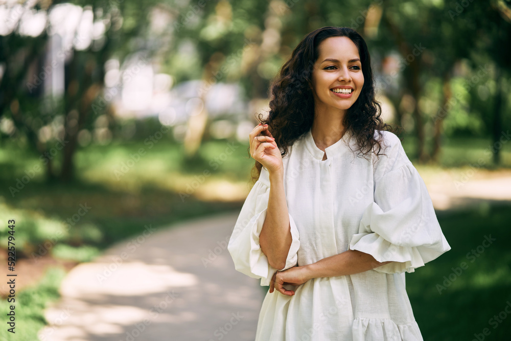 Portrait of a beautiful curly-haired brunette girl in the park. Girl smiling and holding her hair. High quality photo Portrait of a beautiful curly-haired brunette girl in the park. Girl smiling and holding her hair. High quality photo