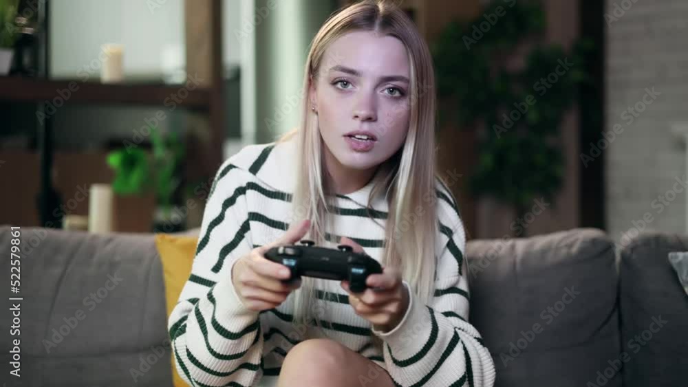 Beautiful excited young gamer girl sitting on a couch and playing in video games on a console. Happy player woman controlling joystick for videogame. Beautiful excited young gamer girl sitting on a couch and playing in video games on a console. Happy player woman controlling joystick for videogame.